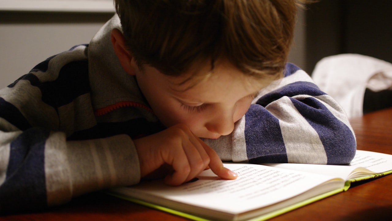 Un bambino che legge seguendo le righe del libro con il dito: uno dei sintomi più comuni della dislessia