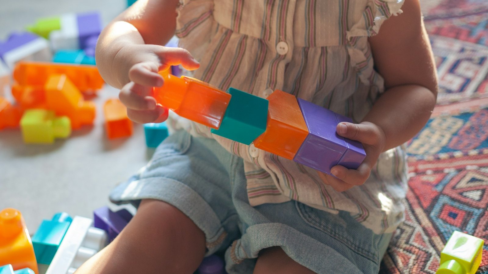 Una bambina piccola incastra cubi colorati uno in fila all'altro: mettere in ordine i giochi, da solo, non è un sintomo di autismo